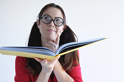 woman wearing glasses holding a book and thinking