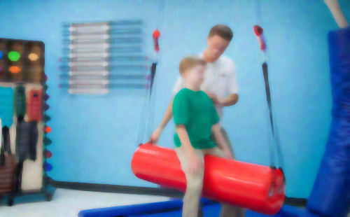 Young boy sitting balanced on a cylinder and receiving physical therapy from specialist