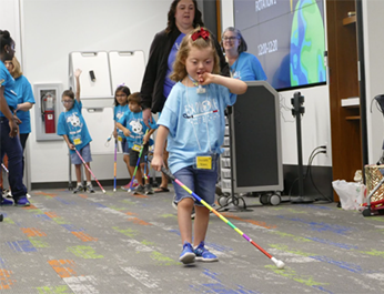 Young girl using white cane while teachers observe