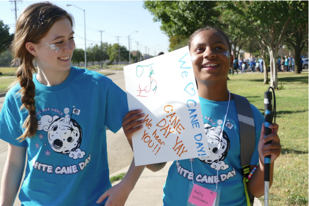 Teacher and student wearing white cane day t-shirts and holding a sign