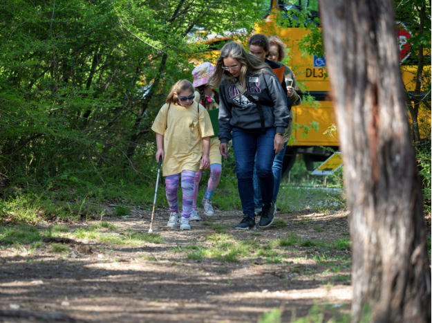 Teacher helping students with white canes exit school bus